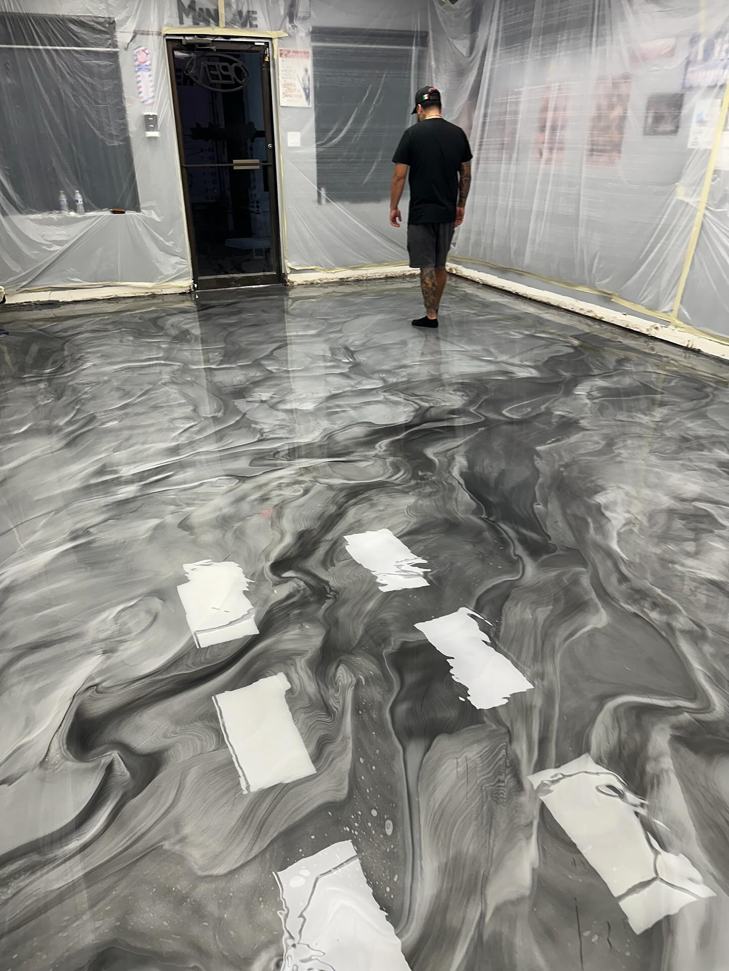 Uriel standing on a fresh grey and black metallic floor, the walls still wrapped in plastic.